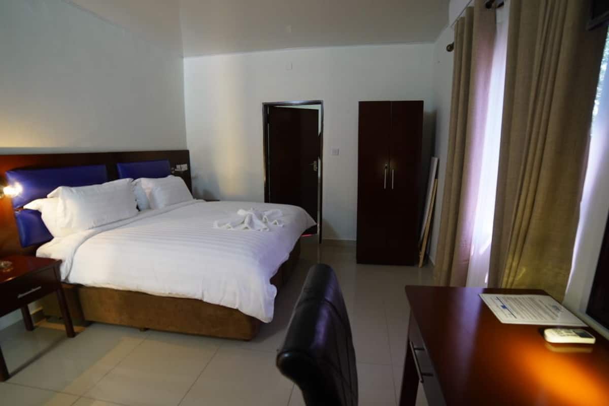 A hotel room with a large bed, a desk, a chair, a wardrobe, and a television.
