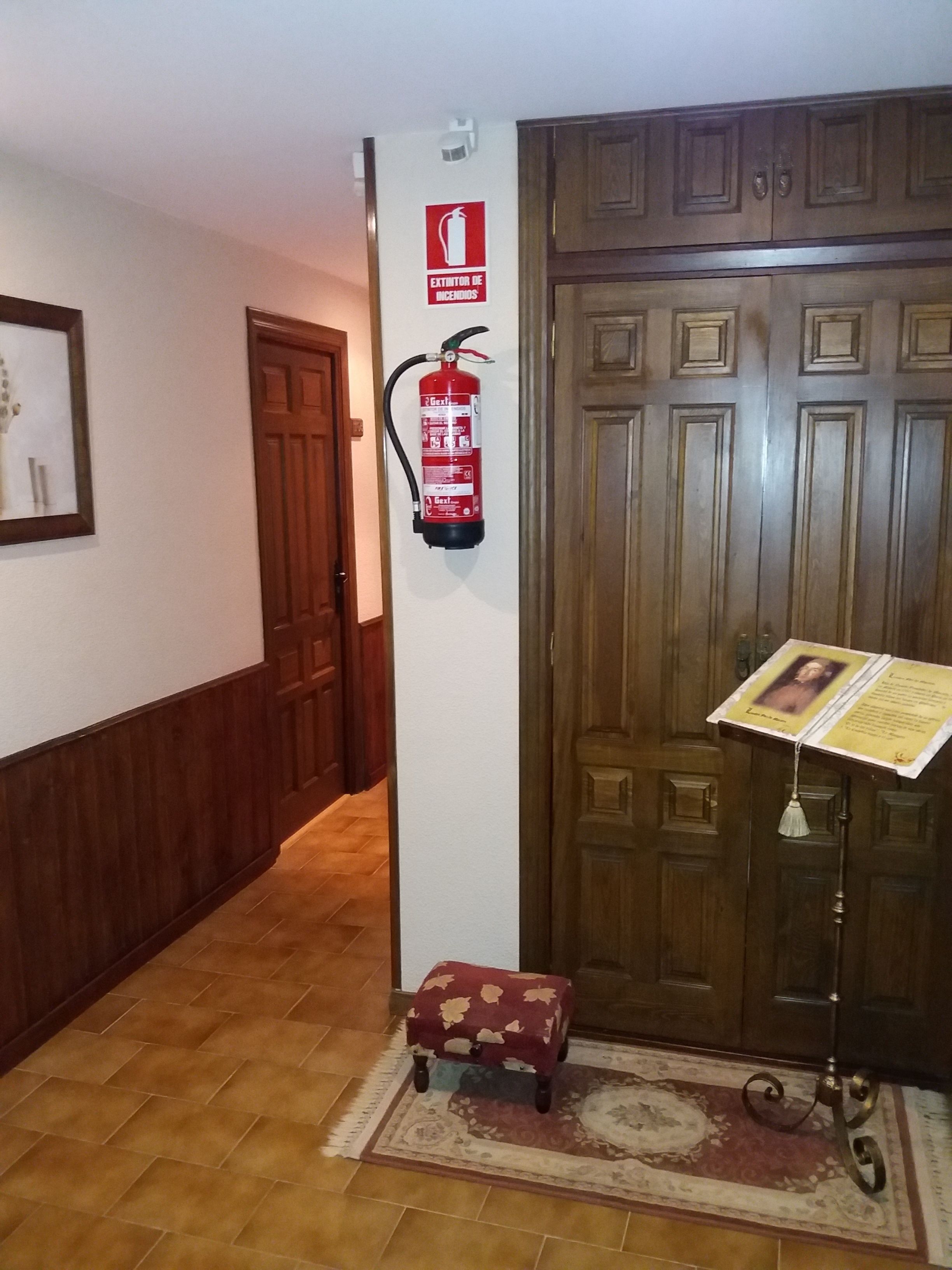 A hallway with a wooden door, a fire extinguisher mounted on the wall, a small bench, and a music stand with sheet music.