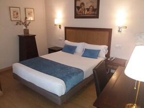 Een hotelkamer met een groot bed, een nachtkastje, een lamp en lijstjes met kunstwerken aan de muren.