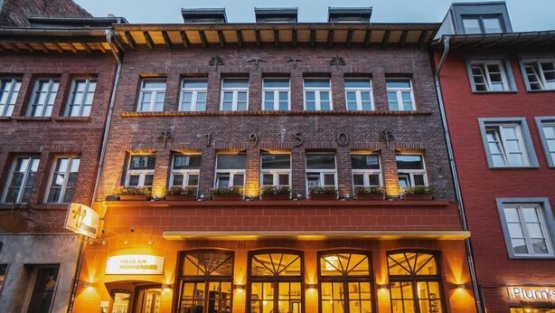 Un bâtiment avec une enseigne indiquant « Haus am Hunnerdiest » et une entrée bien visible, avec une porte et des fenêtres.