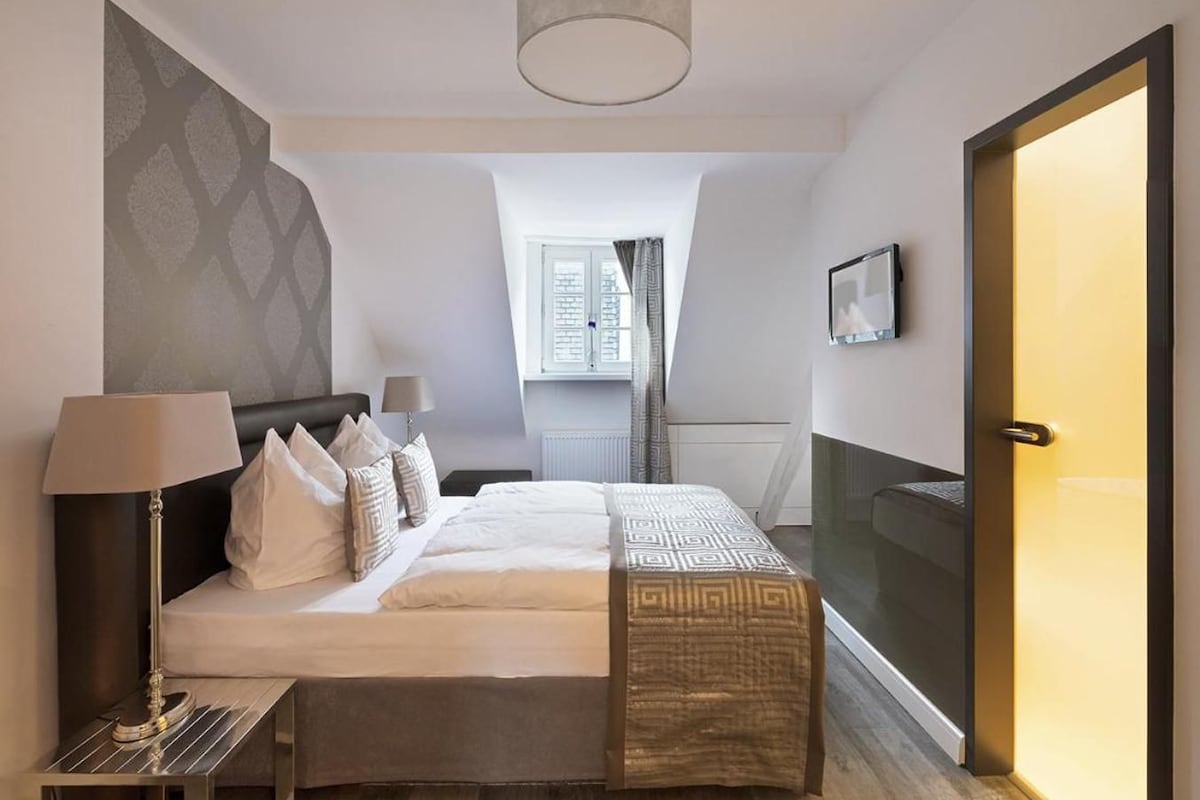 Una habitación de hotel moderna con una cama grande, una mesita de noche, una lámpara, vistas a la ciudad y una puerta corredera.