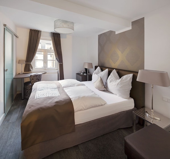 A hotel room with a large bed, a desk, a chair, a nightstand, and a lamp. - Boardinghouse Haus Am Hühnerdieb (Aachen)