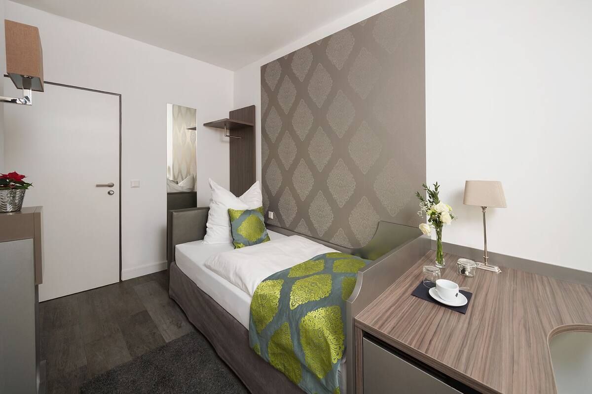 Quarto de hotel com cama, escrivaninha, espelho e parede com desenho decorativo.