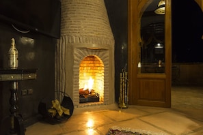 A stone fireplace with a fire, a wooden door, and a metal sculpture.