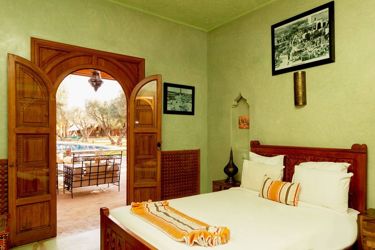 A bedroom with a wooden bed, a view of the pool, and a door leading outside.