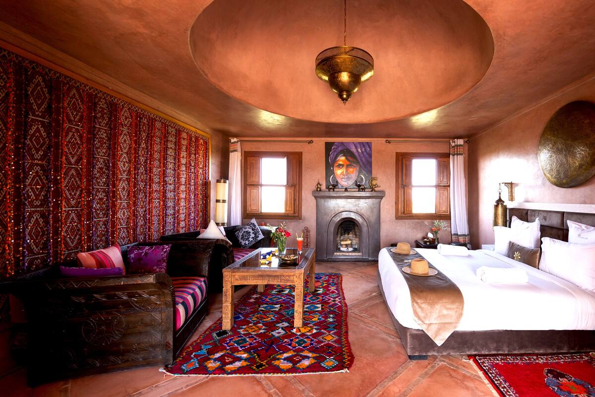 A traditional room with a sofa, a bed, a fireplace, and a patterned wall.