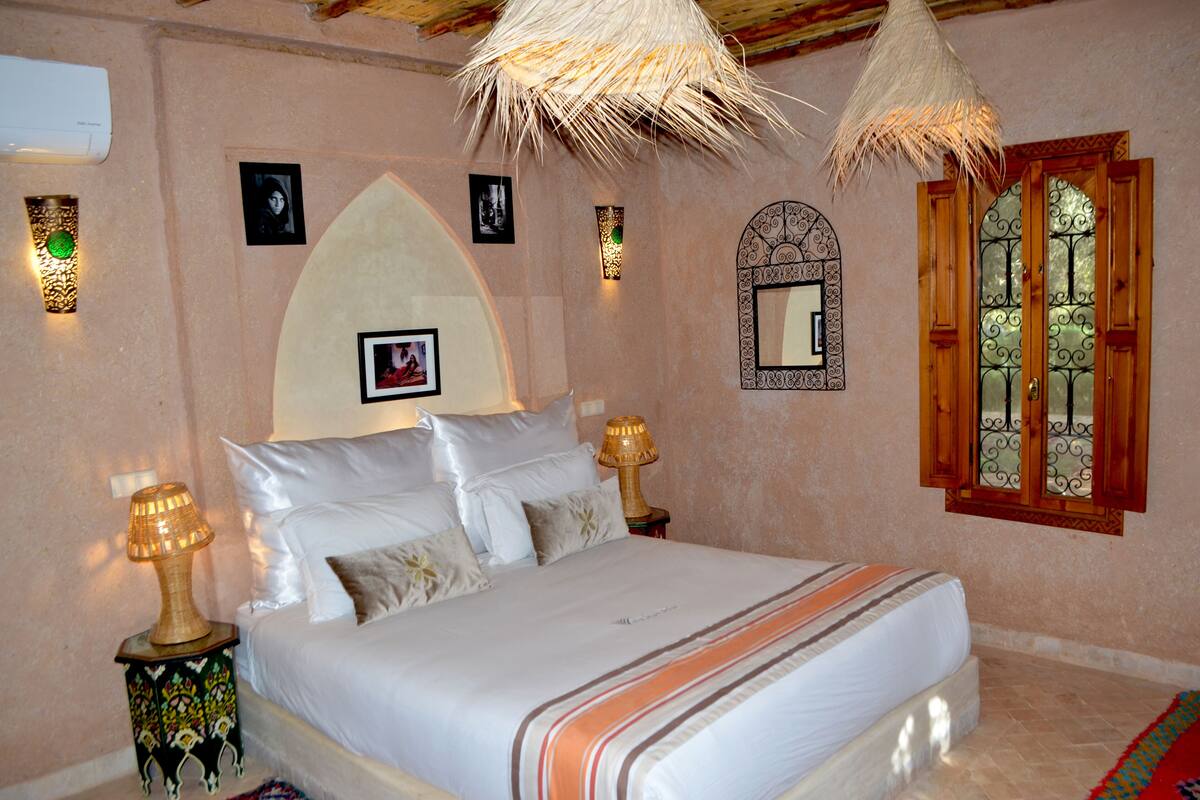 A bedroom with a bed, two bedside lamps, a wall-mounted mirror, and a decorative wall panel.