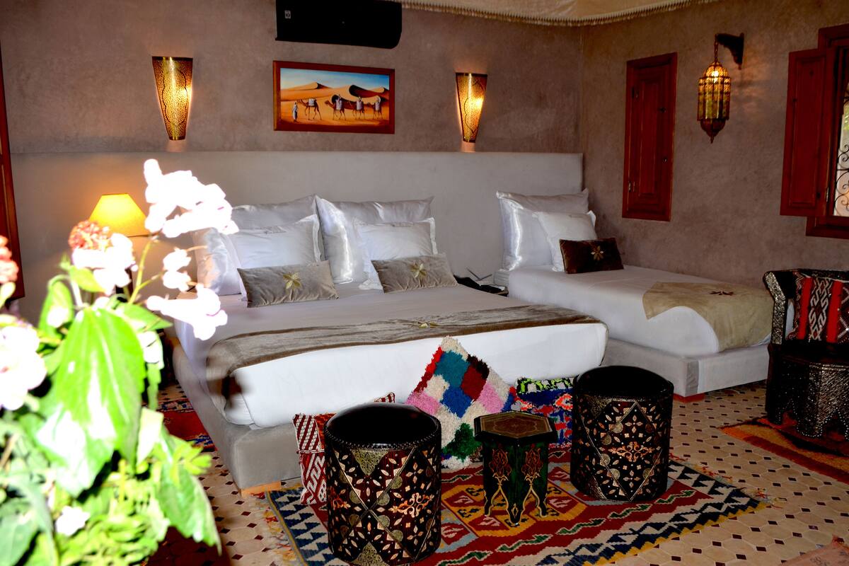 A bedroom with a large bed, two bedside tables, a nightstand, a lamp, and a wall-mounted artwork.