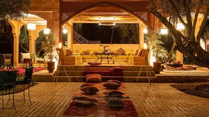 Un espace extérieur aménagé, abrité, avec un canapé et des fauteuils, une table avec une lampe et un tapis décoratif.