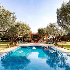 A swimming pool with lounge chairs and umbrellas, surrounded by trees and a covered seating area. - GreenLife Marrakech (Marrakech)