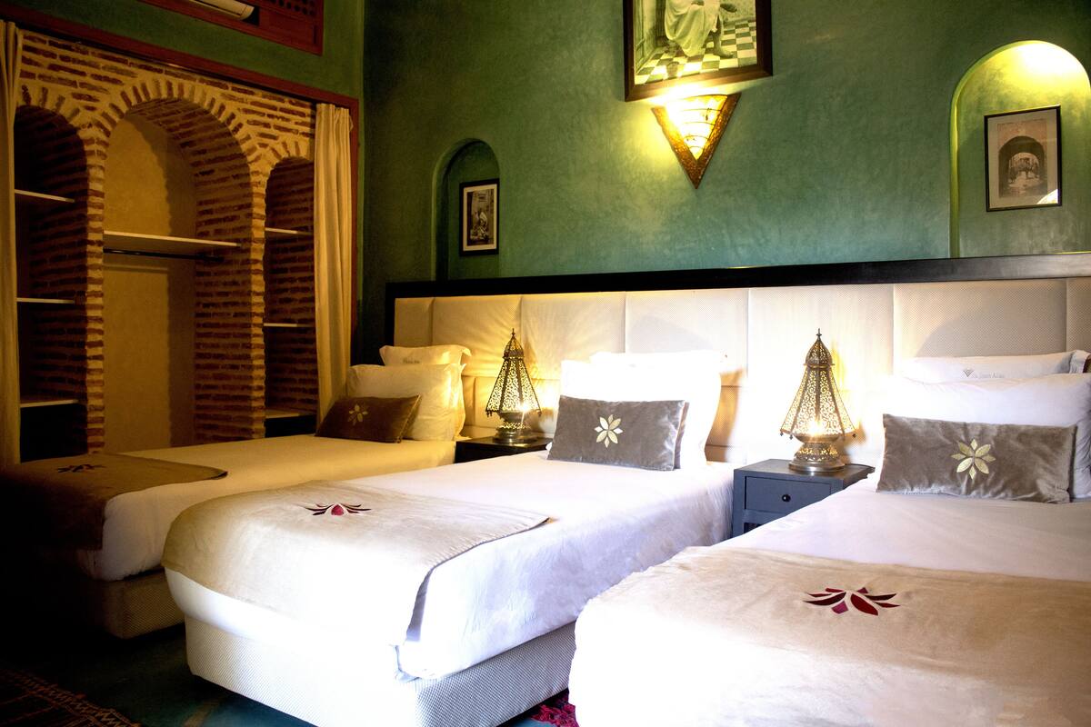 A hotel room with two beds, a brick archway, and a green wall with a framed picture.