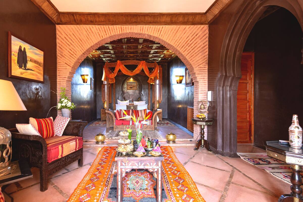 A traditional Moroccan interior with a sofa, a table with a lamp, and a decorative archway.