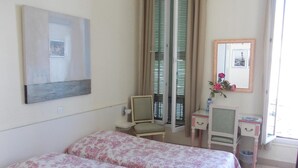 A hotel room with two beds, a small desk, a chair, a mirror, and a window with curtains. - Hôtel l'Oursin (Saint-Jean-Cap-Ferrat)
