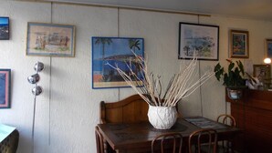 A dining area with a wooden table, chairs, and a white vase with branches. There are framed pictures on the wall. - Hôtel l'Oursin (Saint-Jean-Cap-Ferrat)