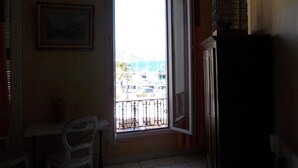 A room with a window, a chair, a table, a framed picture, and a birdcage. - Hôtel l'Oursin (Saint-Jean-Cap-Ferrat)