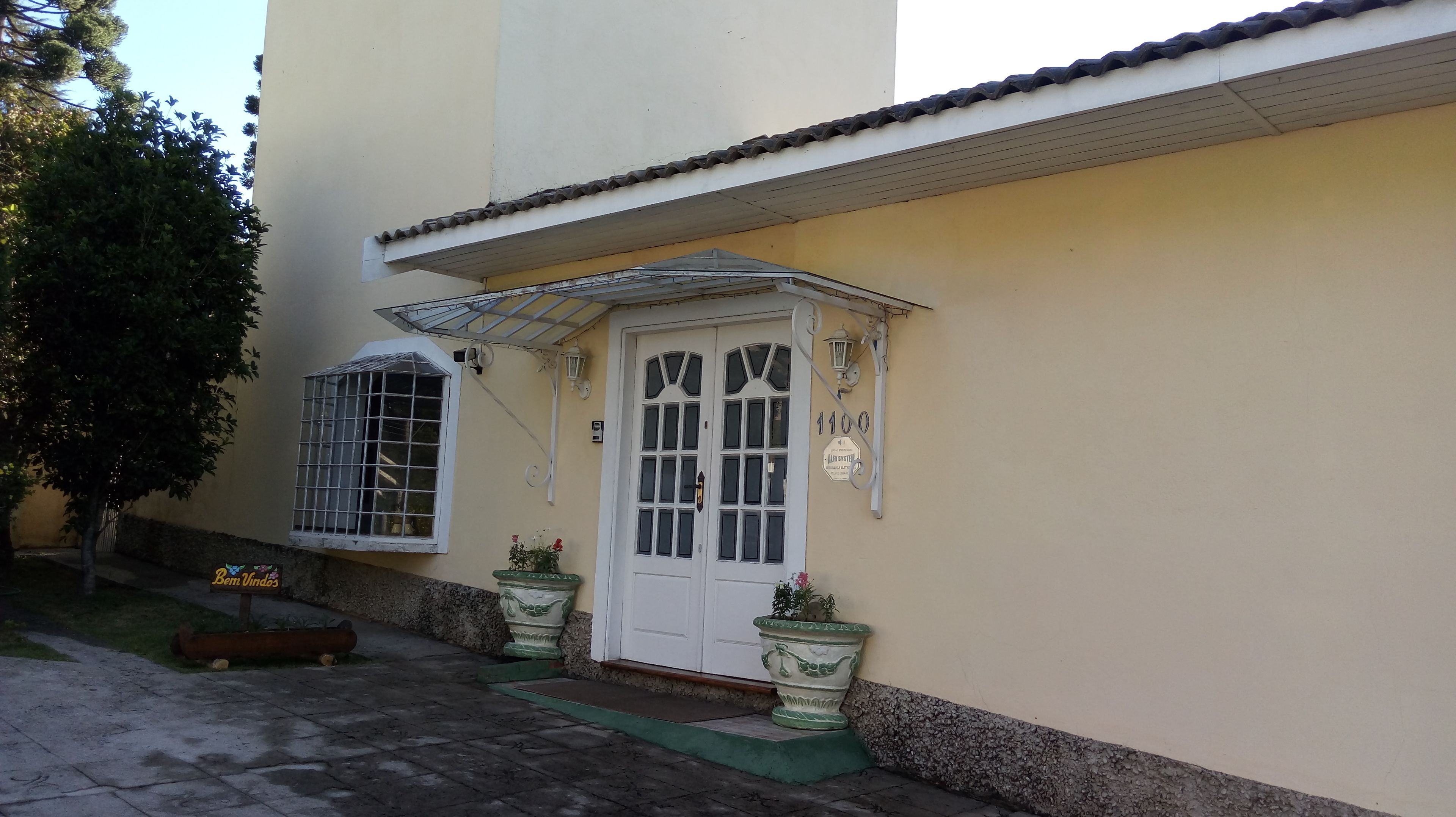Um edifício com porta e janelas brancas, um pequeno alpendre e plantas em vasos.