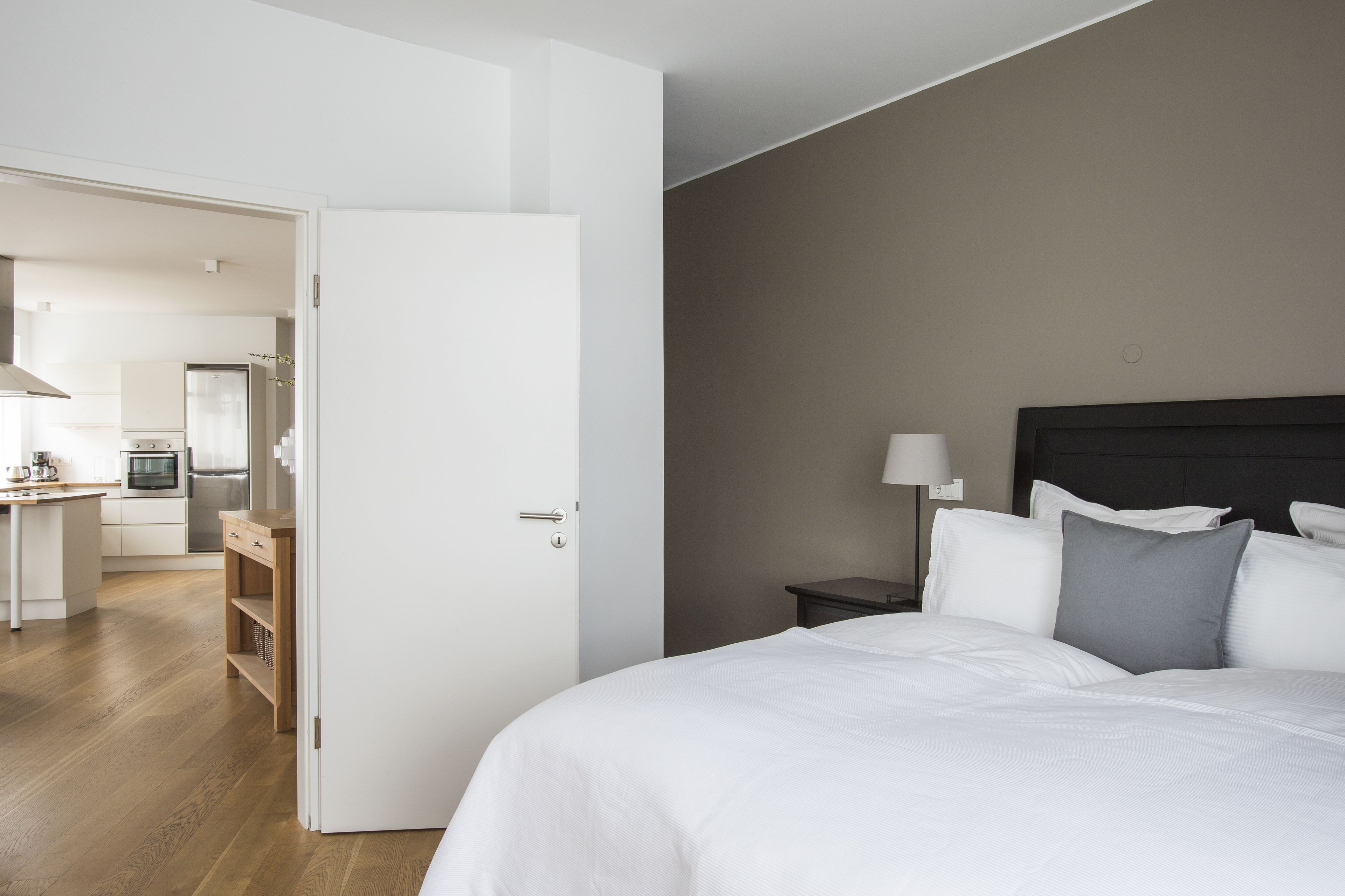 A hotel room with a bed, bedside table, and a view of the kitchen area.