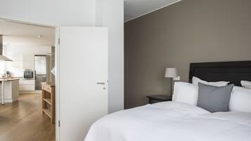 A hotel room with a bed, bedside table, and a view of the kitchen area.