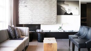 Un salon moderne avec un canapé, une table basse et un fauteuil en cuir. On y trouve un mur en briques et un grand tableau encadré.