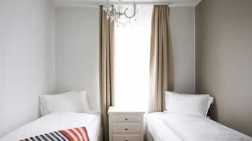 A bedroom with two beds, a nightstand, a chandelier, and beige curtains.