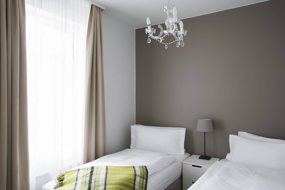 Een hotelkamer met twee bedden, een kroonluchter, een bedlampje en een raam met gordijnen.