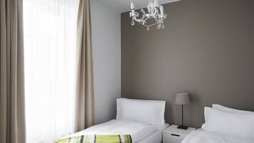 Habitación de hotel con dos camas, una araña, una lámpara de noche y una ventana con cortinas.