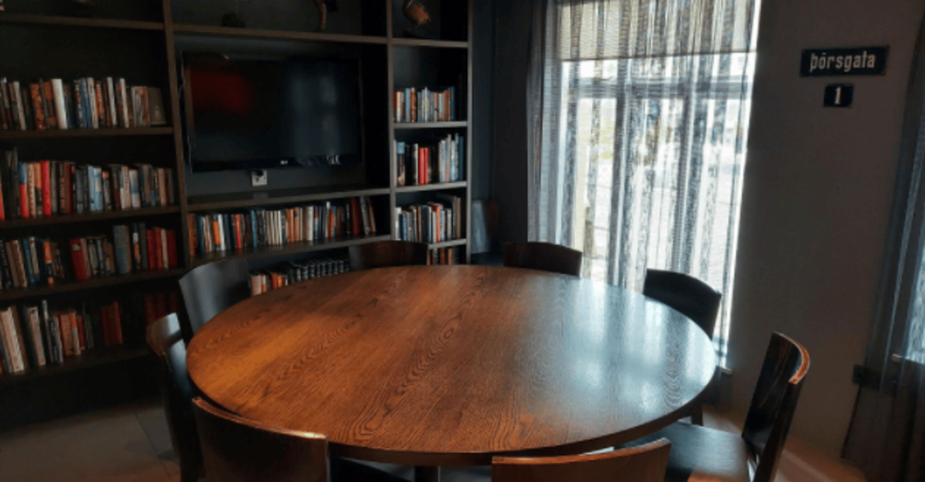 A round wooden table surrounded by chairs in a room with bookshelves and a television.