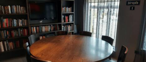 A round wooden table surrounded by chairs in a room with bookshelves and a television.
