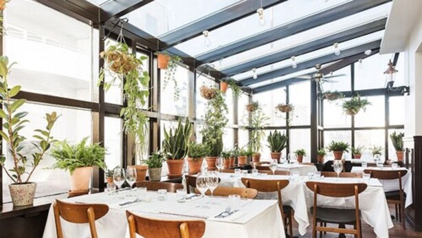 Un restaurant avec des tables dressées pour le service, des plantes en pot et des plantes suspendues.