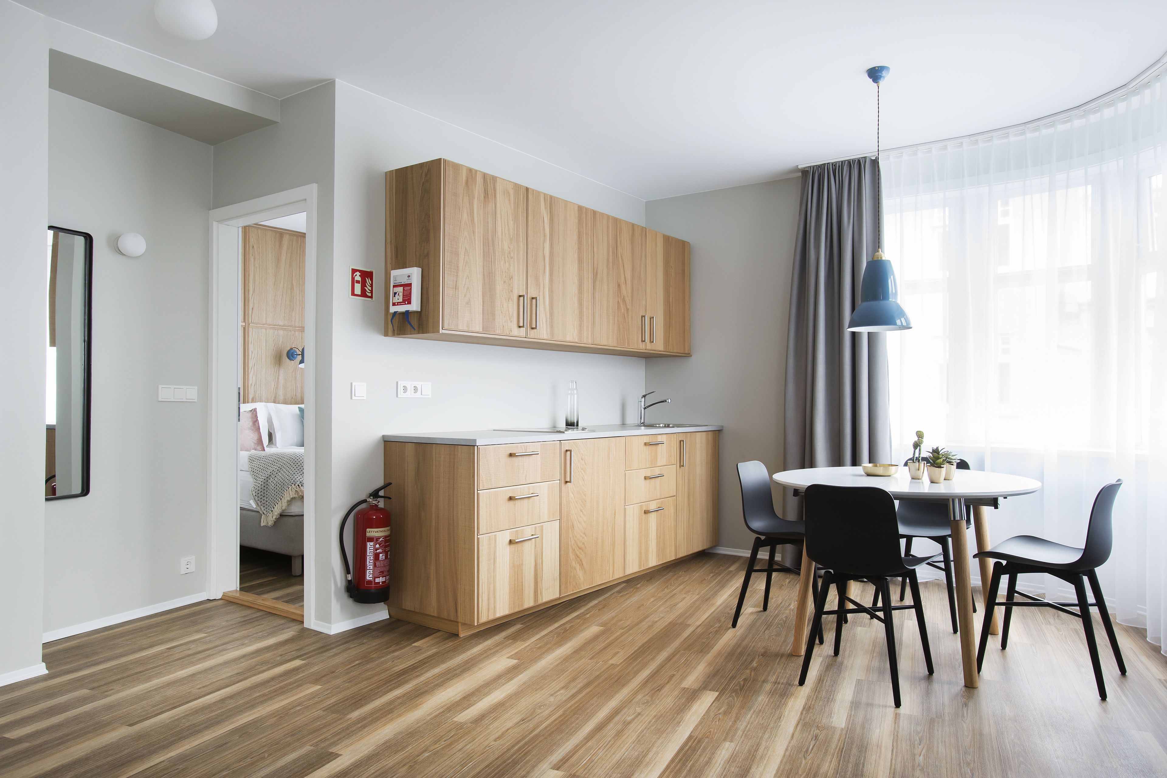 A modern kitchen with wooden cabinets, a dining table with chairs, and a visible fire extinguisher.