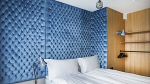 Une chambre à coucher avec une tête de lit capitonnée, un lit avec du linge de lit blanc, une table de chevet avec une lampe et une armoire en bois.