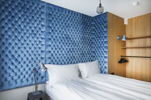 A bedroom with a tufted headboard, a bed with white linens, a nightstand with a lamp, and a wooden wardrobe.