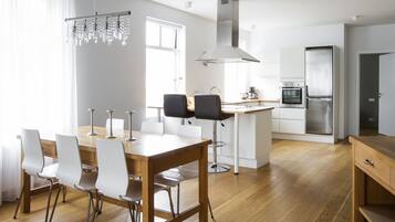 A modern kitchen with a wooden dining table, white chairs, stainless steel appliances, and a hanging light fixture.