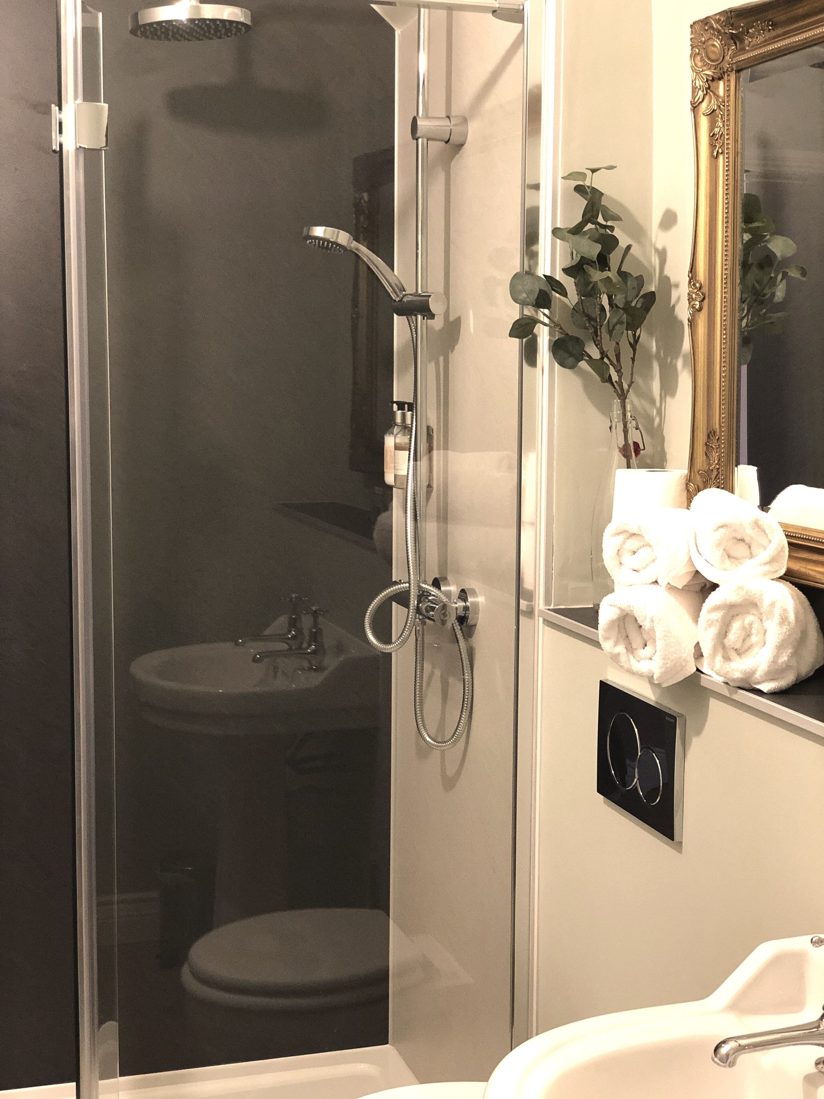Een badkamer met een douche met glazen wanden, een wastafel en een spiegel met decoratieve lijst.