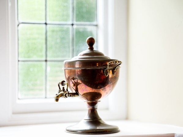A brass teapot with a spout and handle on a white table near a window. - The Wheatsheaf (Milnthorpe)