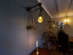 A room with a wooden table, a lit candle, and wall-mounted lighting fixtures. - The Wheatsheaf (Milnthorpe)