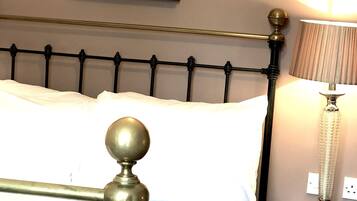 Una cama con estructura de metal negro y detalles en latón, una mesita de noche con una lámpara, y un cuadro enmarcado en la pared.