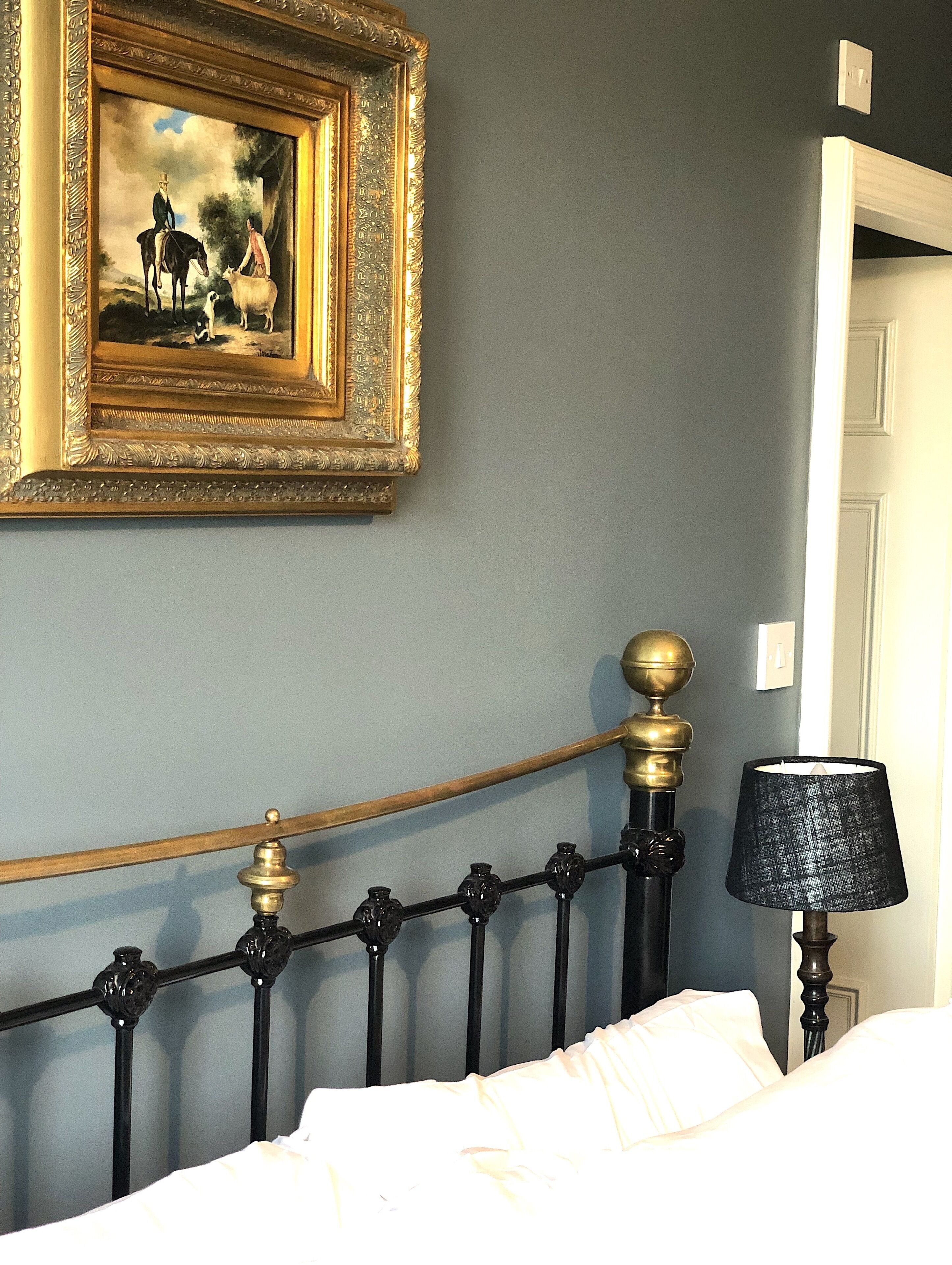 A bedroom with a bed, a lamp, a metal headboard, and a framed painting on the wall.