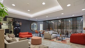 Una sala moderna con sofá, reposapiés y mesa de centro, una estantería, y un comedor con sillas y mesa.