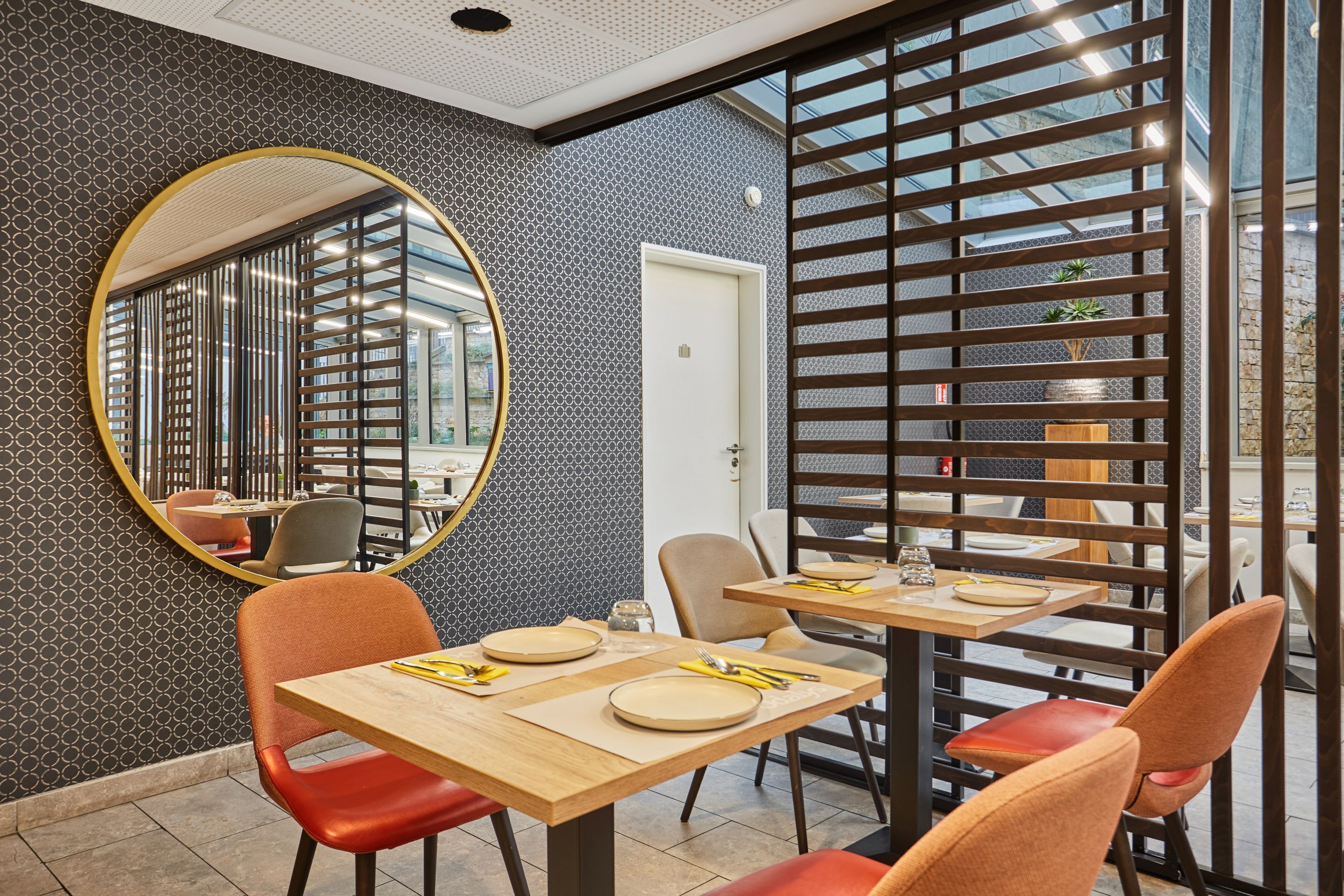 A dining area with wooden tables and chairs, a large mirror, and a patterned wall.