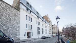 Vista de la calle con un edificio que dice 'ODAL'S CITY', con fachada de piedra, un edificio blanco con múltiples ventanas y coches estacionados.