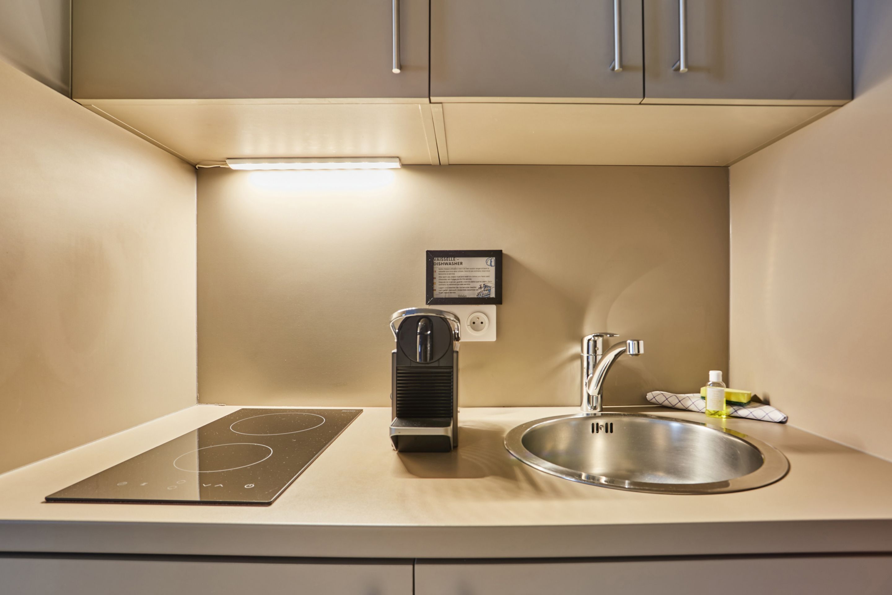 A compact kitchenette with an induction cooktop, a built-in sink, and a compact dishwasher.