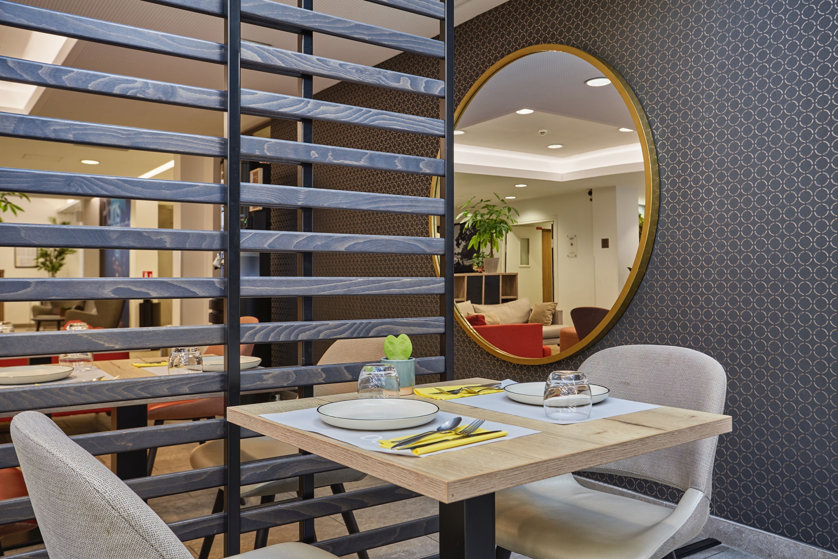 A dining area with a table set for two, a mirror, and a view of the interior space.