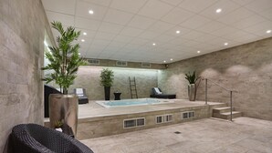 Un área de piscina interior moderna con un jacuzzi, sillones de descanso y plantas en macetas.