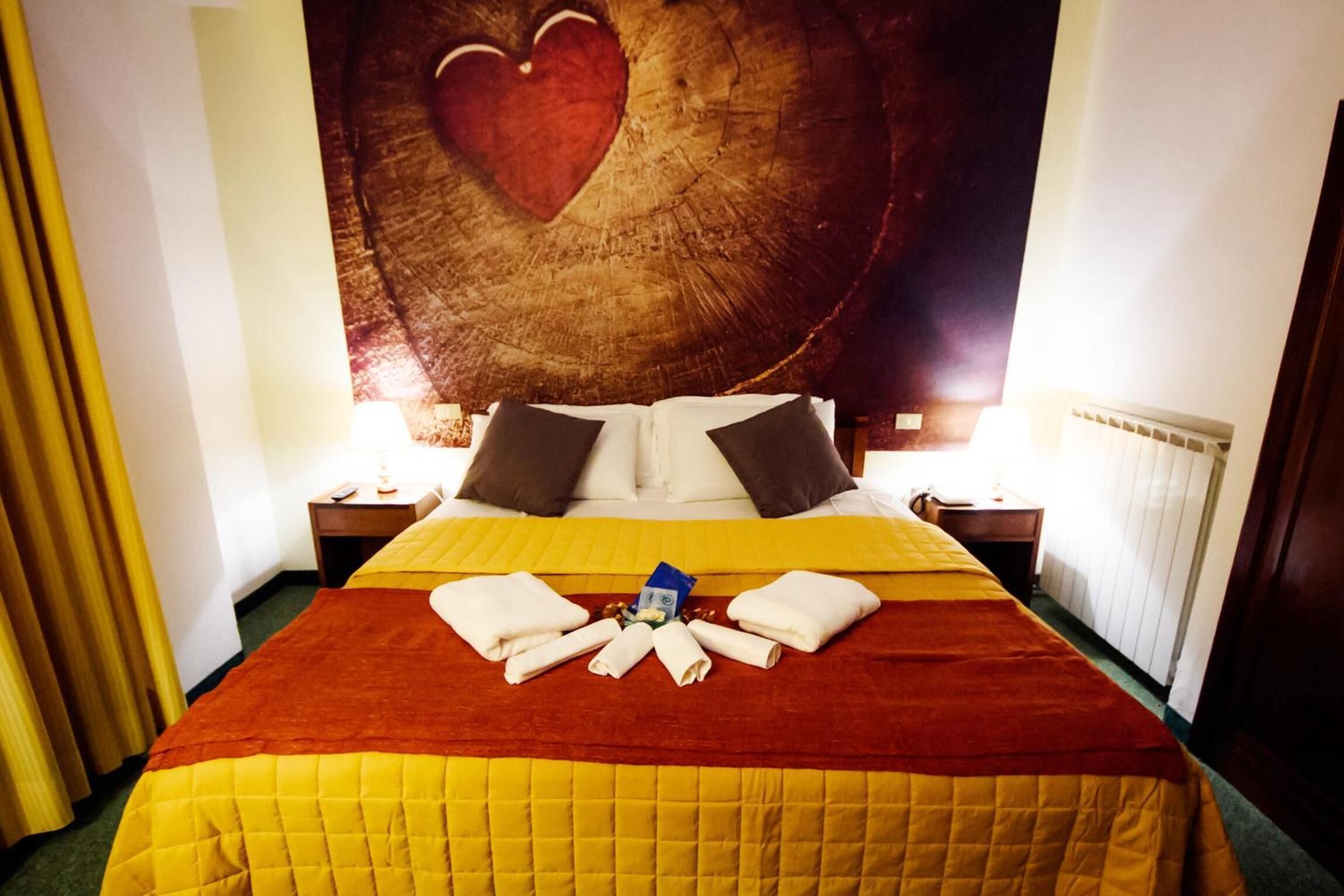 A hotel room with a large bed, a heart-shaped wall decoration, and a neatly arranged towel on the bed.