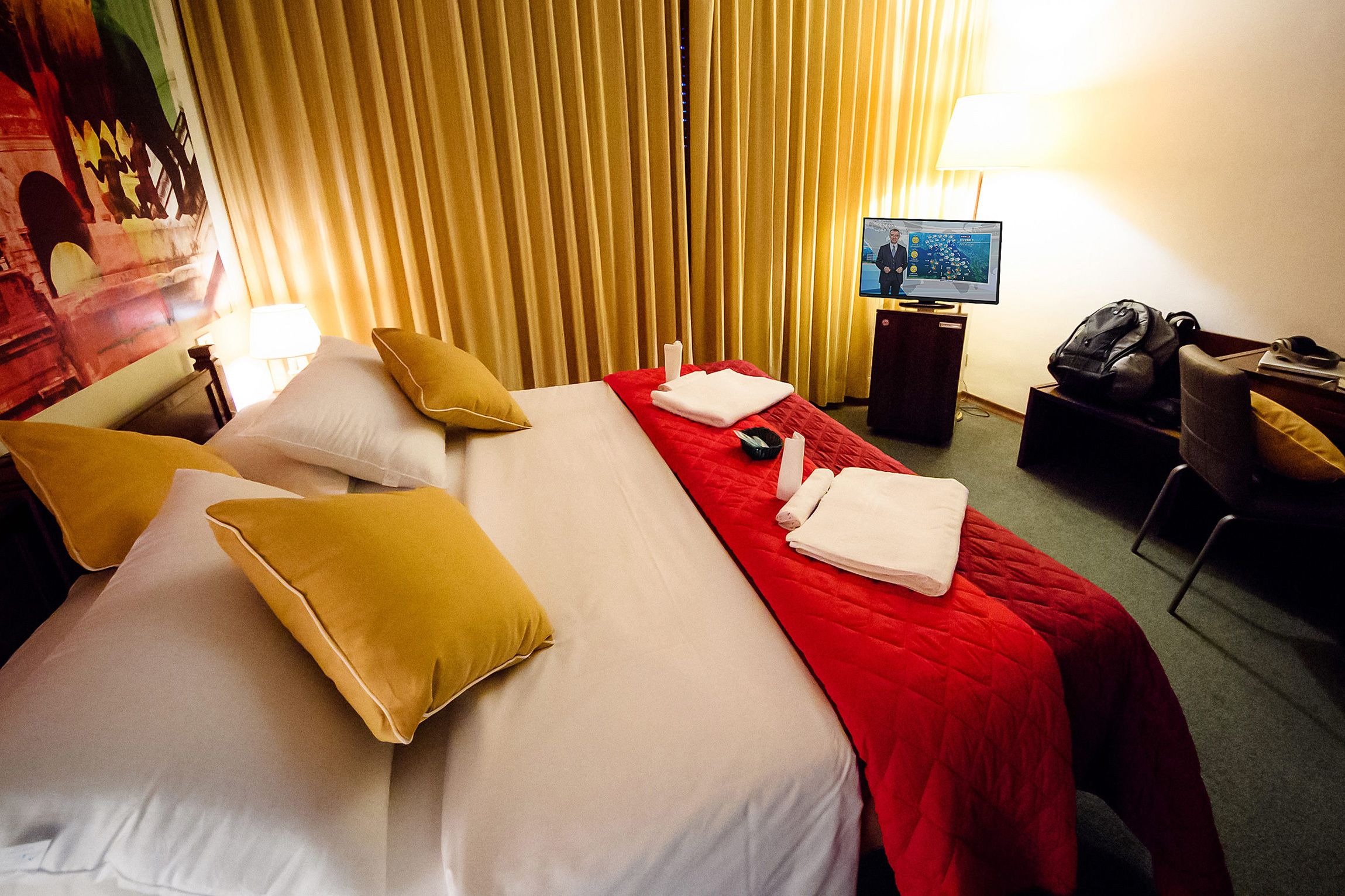 A hotel room with a bed, pillows, a TV, a desk, and a chair.
