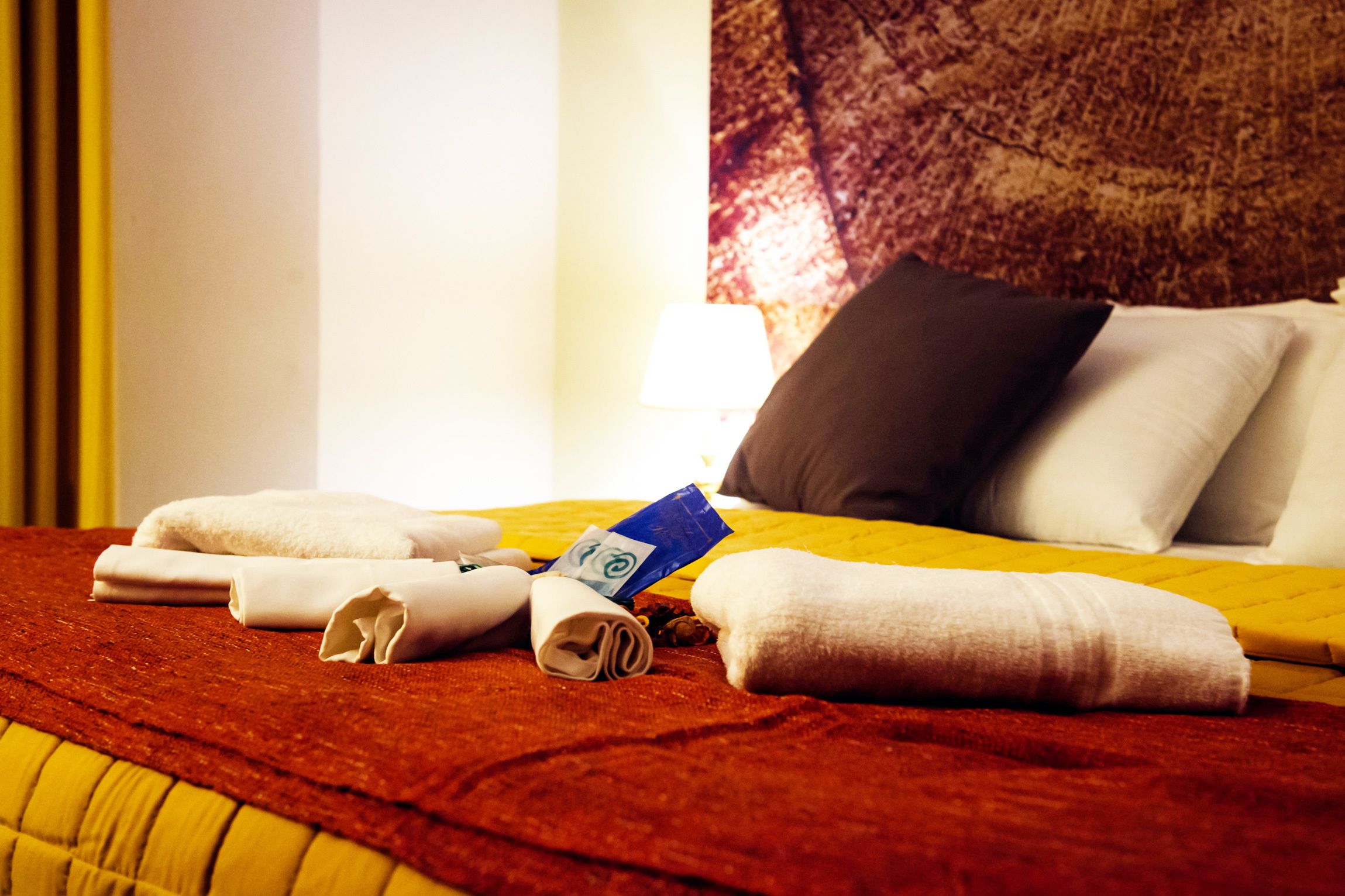 Un lit bien fait, avec des serviettes pliées, un oreiller et une carte bleue posée sur un couvre-lit jaune.