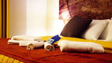 A neatly made bed with rolled towels, a pillow, and a blue card on a yellow bedspread.