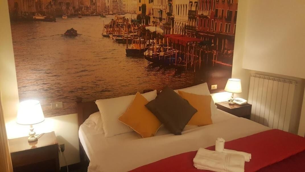 Une chambre d’hôtel avec un lit, des oreillers, une couverture rouge et une vue sur un canal où naviguent des bateaux.