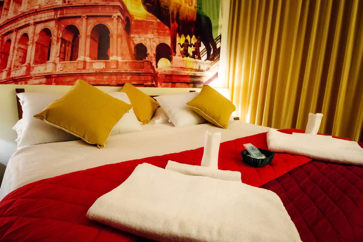 Ein Hotelzimmer mit einem Bett, ausgestattet mit roter und weißer Bettwäsche, mehreren Kissen und ordentlich gefalteten Handtüchern.